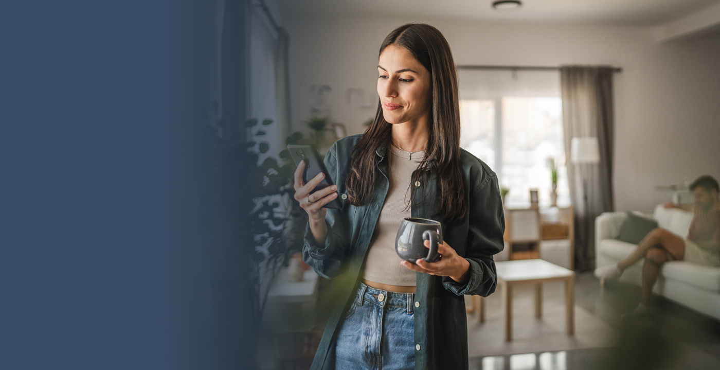 Woman on her phone in her house with coffee in hand